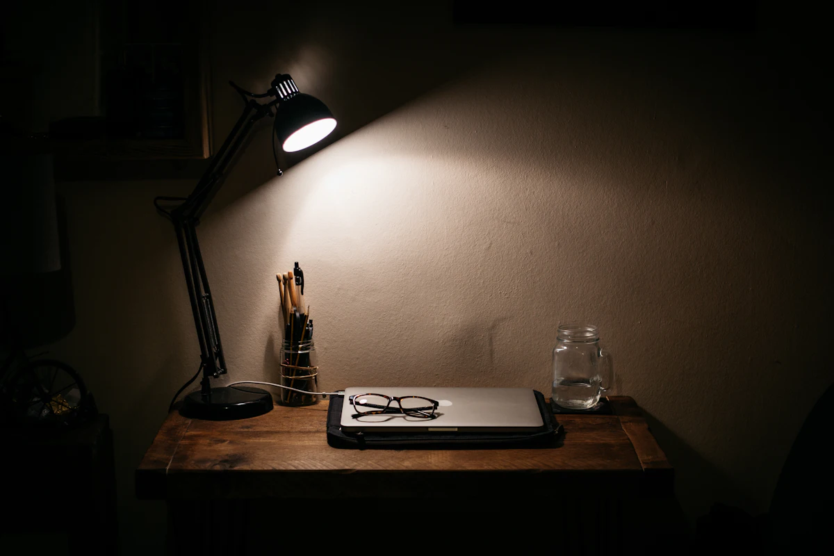 Ruhiger Schreibtisch mit Lampe, zugeklapptem Laptop und Brille